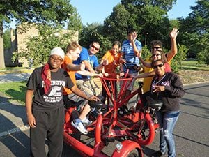 Group of young adults play on bicycle that has multiple seats and pedals.