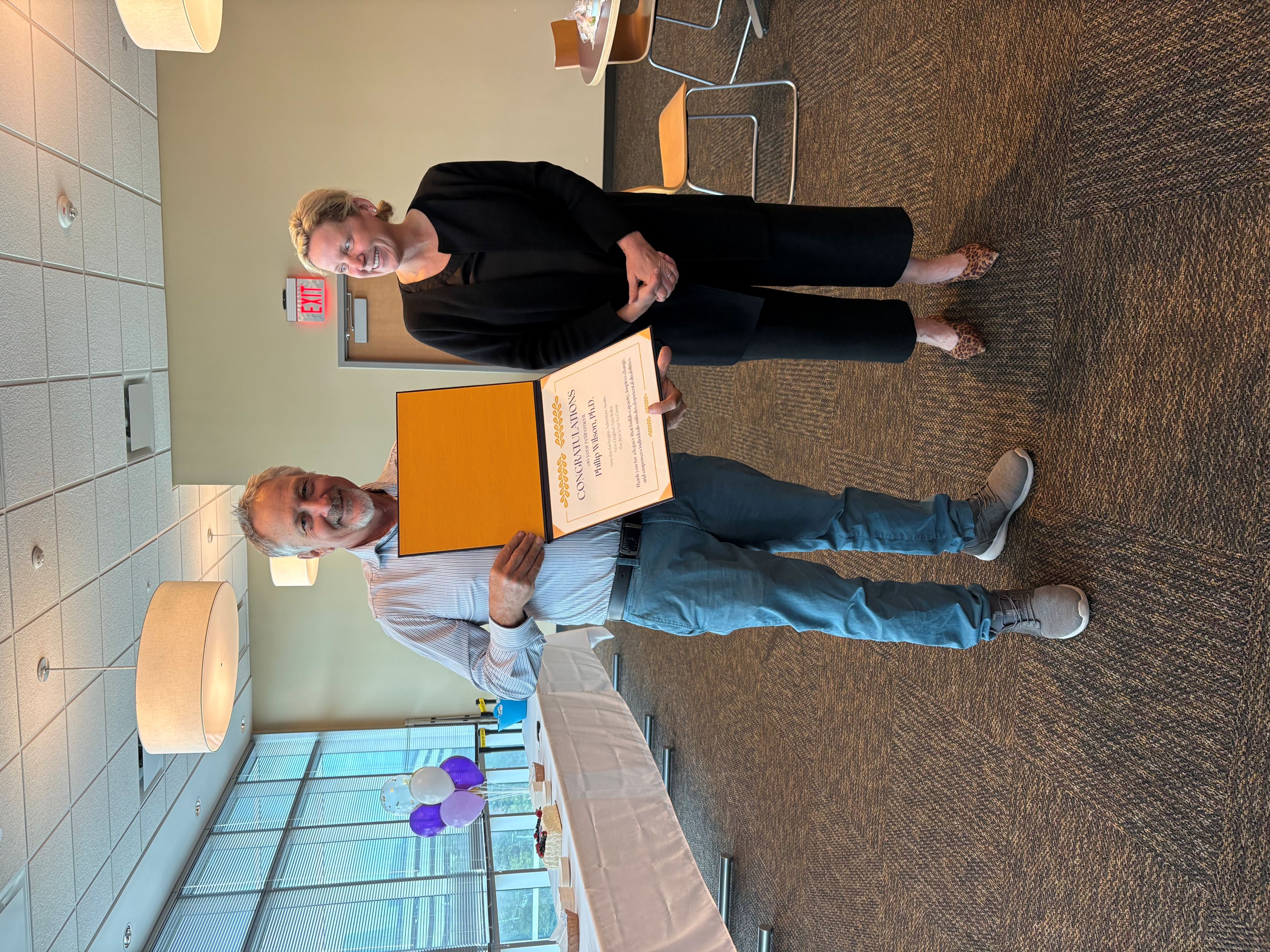 Dr. Wilson holds congrautlatory certificate as Dr. Dean smiles looking at him.