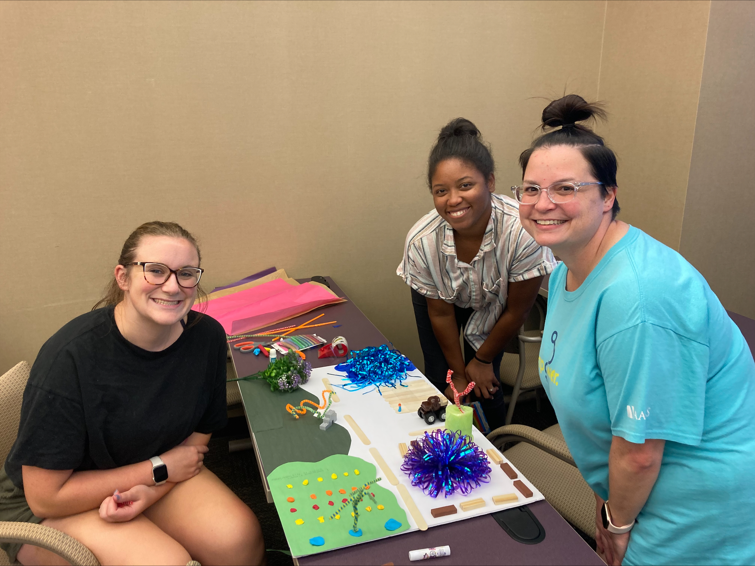 Three LEND Scholars with a group project that shows a community build out of arts and crafts.