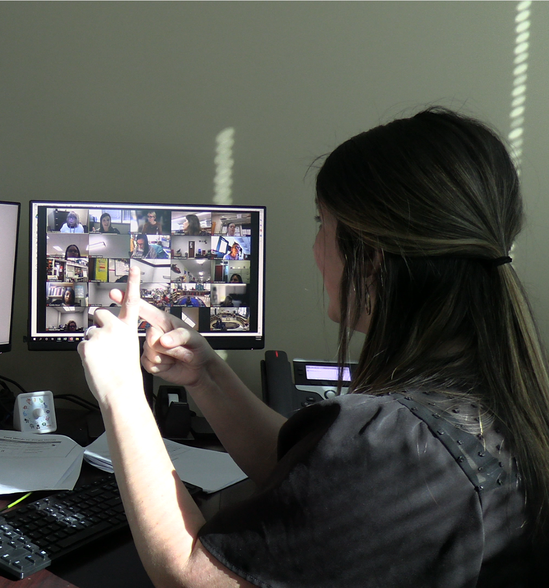 Woman gestures number 1 with her hand as she presents to a virtual group displayed on her computer.
