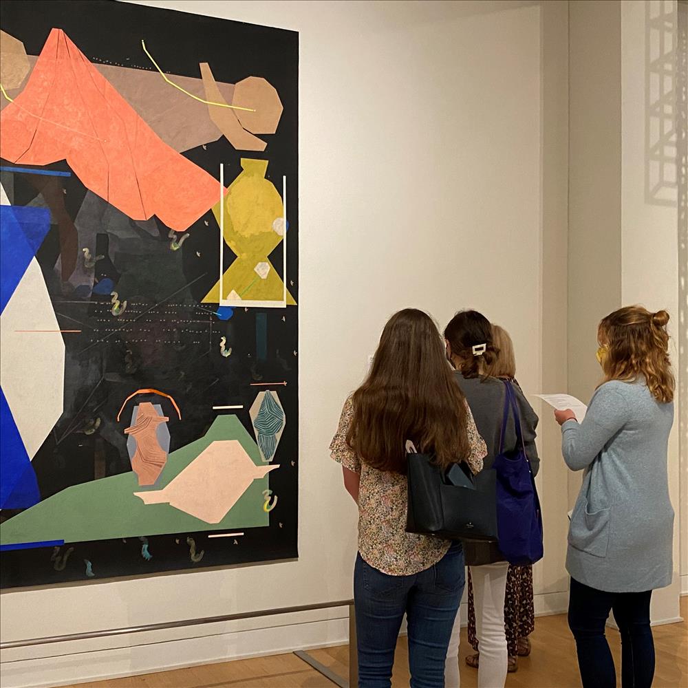 Young women looking at something next to landscape picture formed by collage