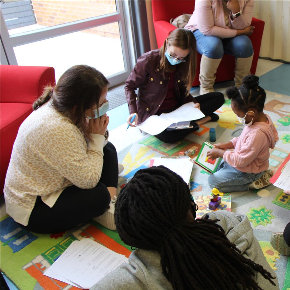 HDC staff and LEND scholar interact with child in classroom who is looking at book