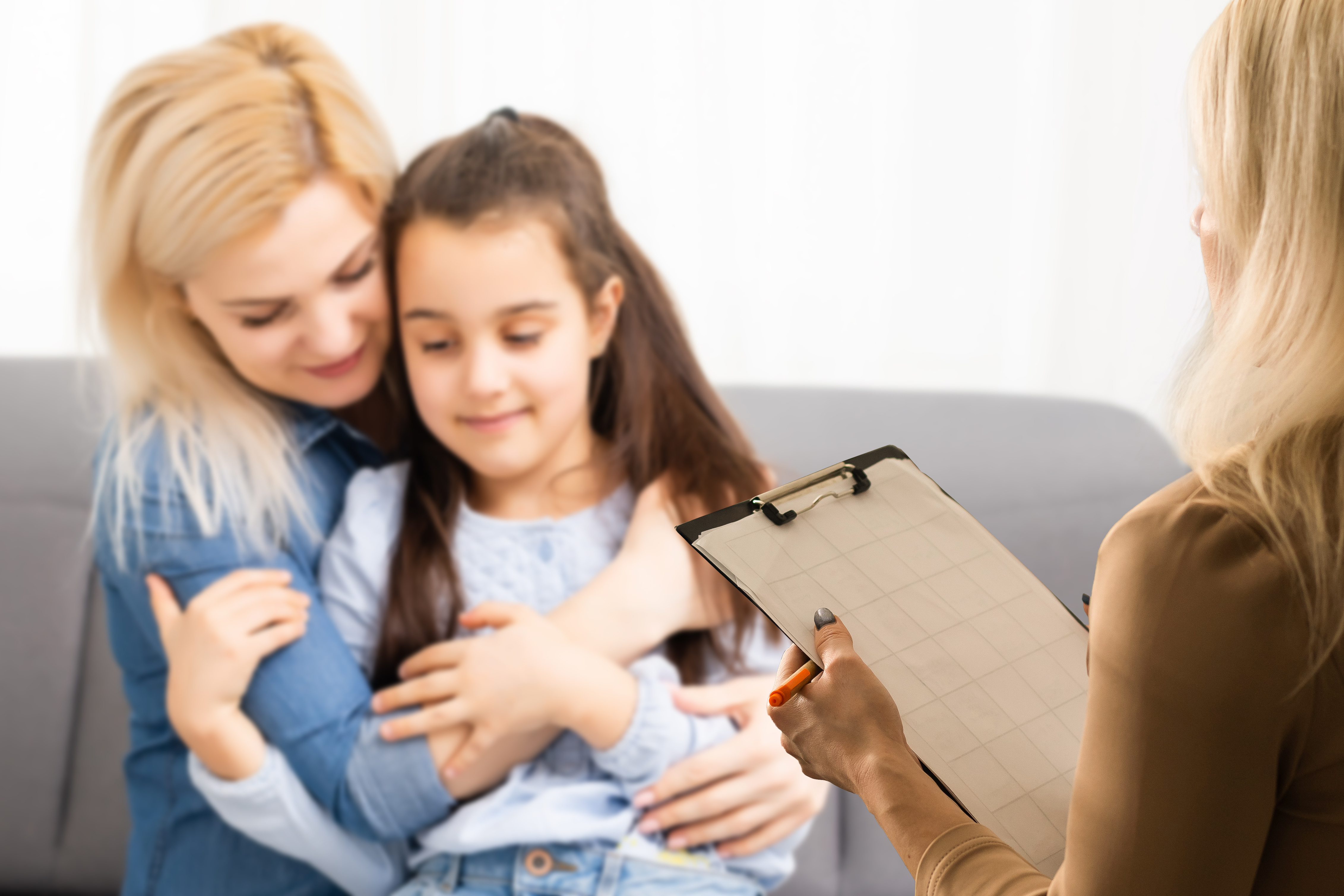 Therapist with clipboard speaks to mother as she hugs her young daughter.