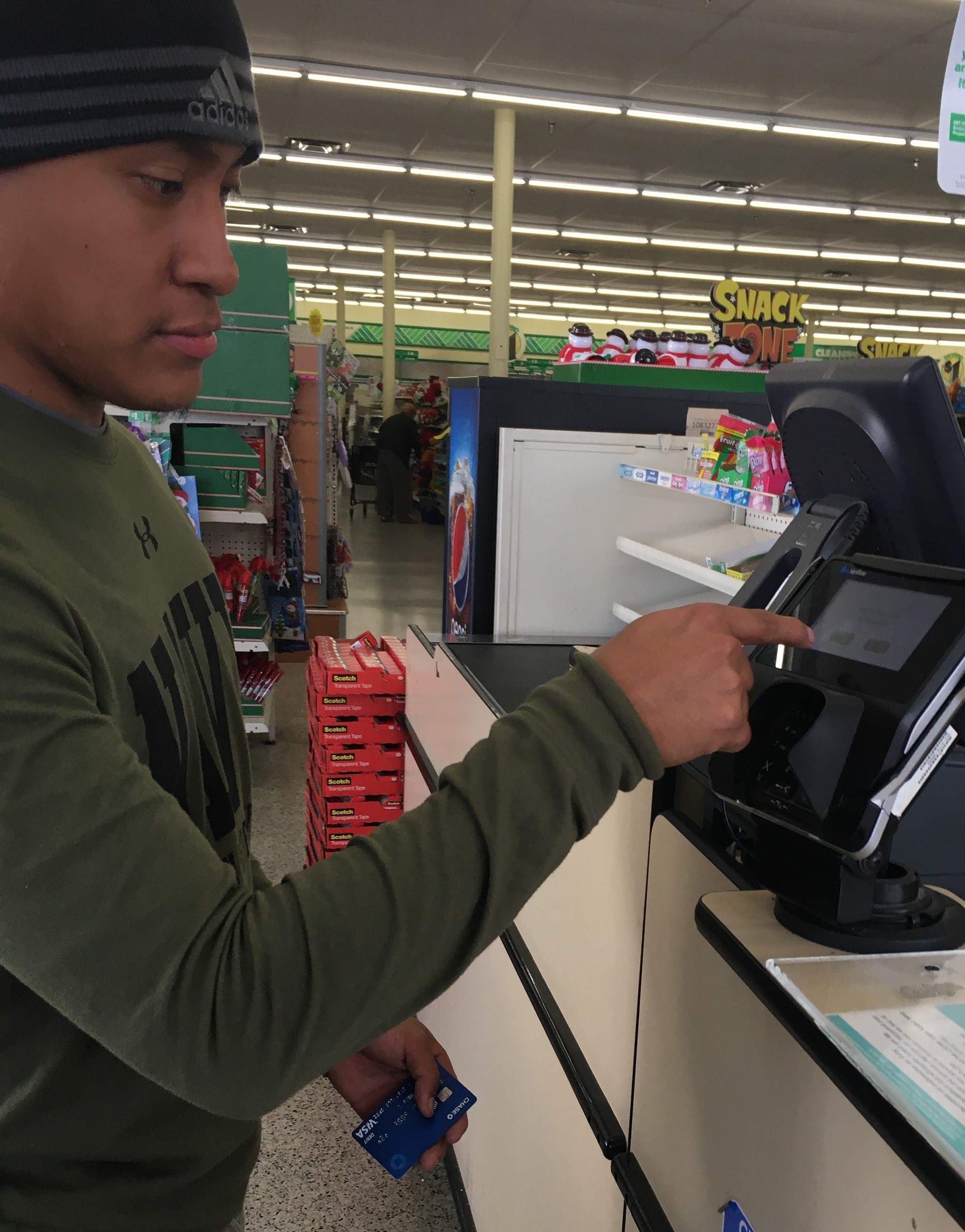 A young man swipes credit card at grocery store register.