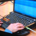 White person's hand using a computer with blue faint screen equipped with JAWS screen reader