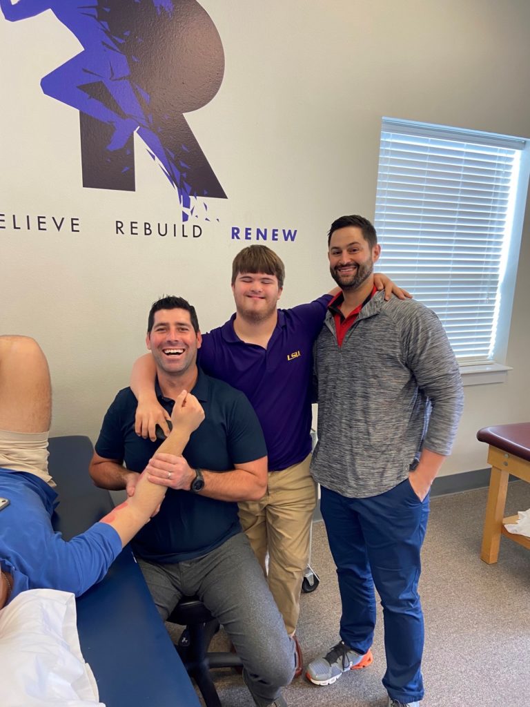 Teenage boy smiles with his arms around his managers at a clinic.