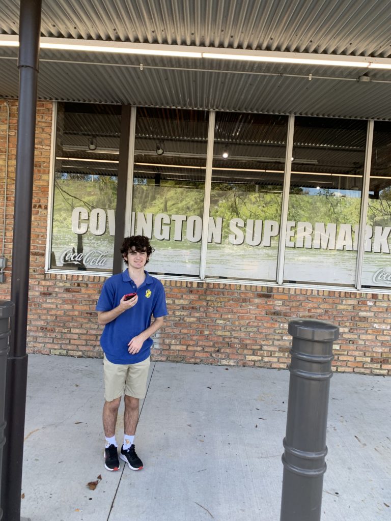 Teenage boy stands with a thumbs up outside a grocery store.