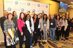 A group of 23 HDC staff and scholars porf3essionally dressed stand in front of an AUCD step and repeat banner.