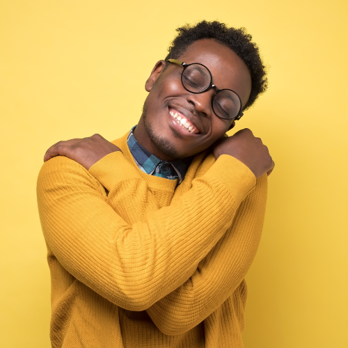 Young man wearing glasses hugs himself with big smile and eyes closed.  