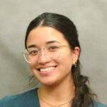 Black-haired Asian woman in clear-framed glasses and teal V-necked shirt