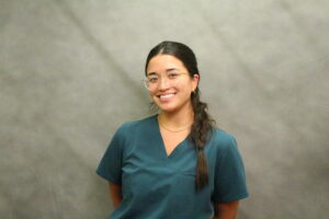 Black-haired Asian woman in clear-framed glasses and teal V-necked shirt