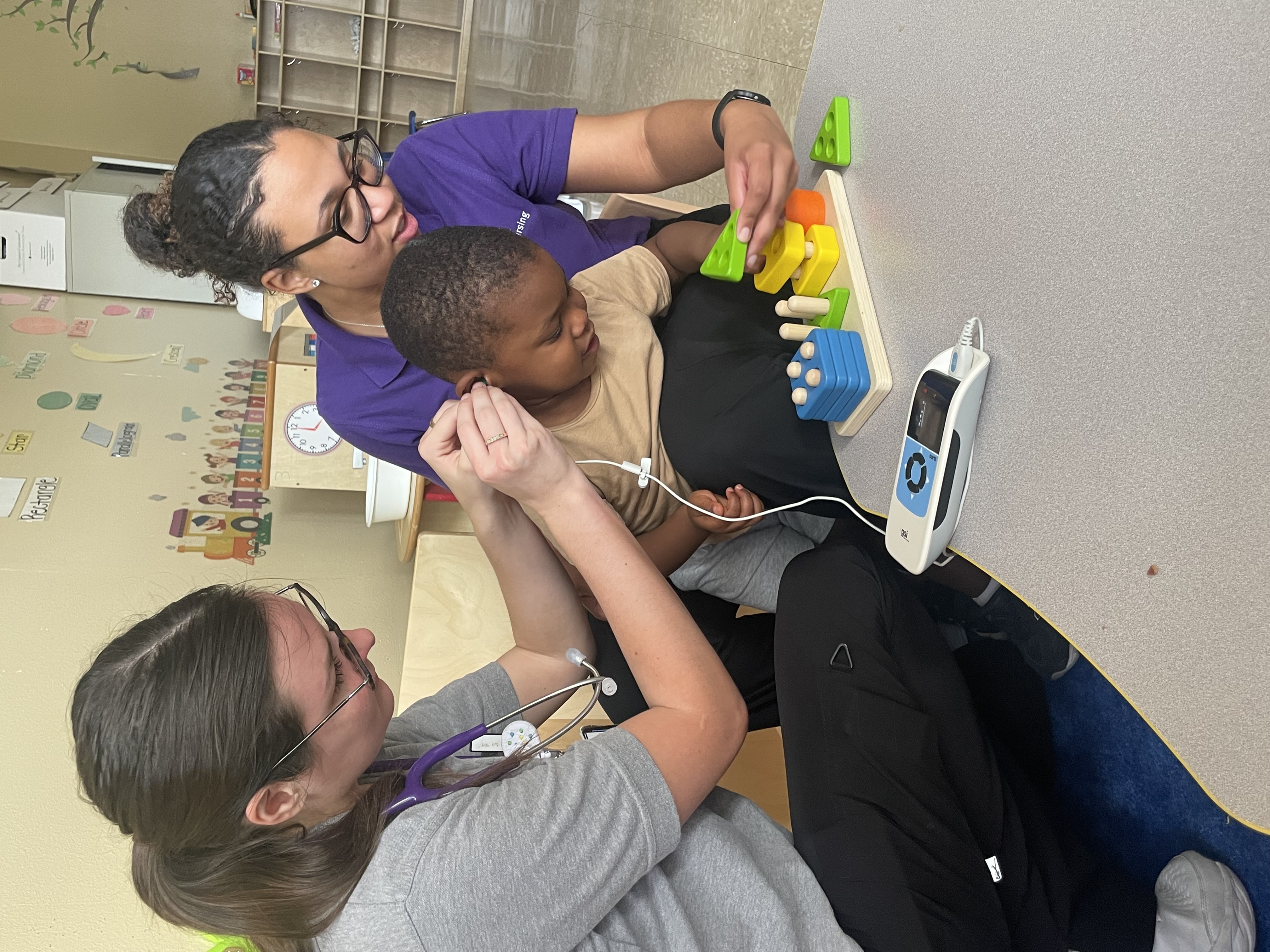 LSUHSC students conduct hearing test on toddler as he plays with blocks in his classroom.